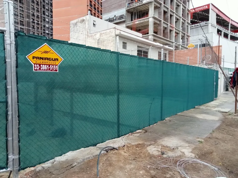 Alambrado con malla sombra verde y placa Paniagua junto a una obra