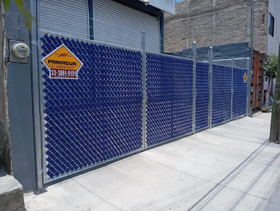 Portón de malla ciclónica con cinta de privacidad azul y placa Paniagua