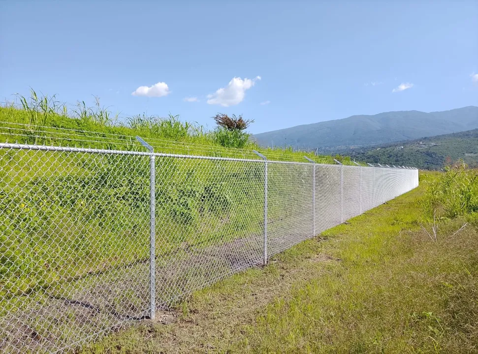 Malla ciclónica delimitando un terreno en el campo con montañas al fondo