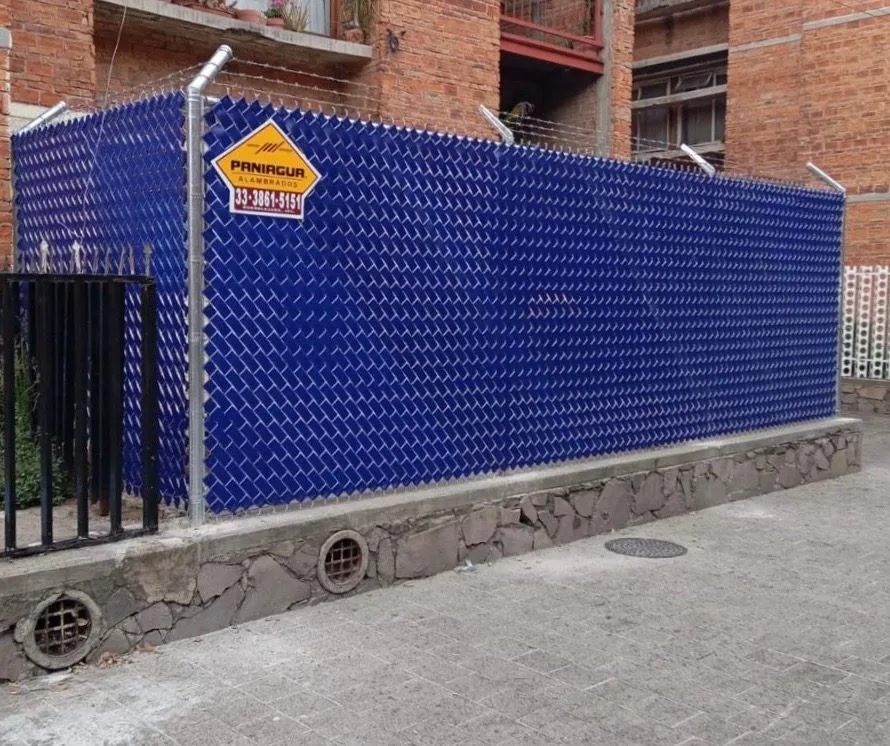 Malla con cinta de privacidad azul sobre una barda de piedra con placa Paniagua