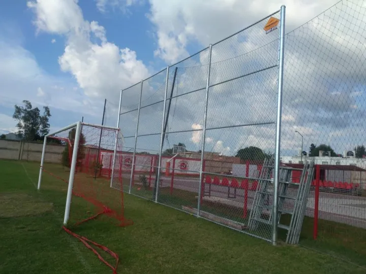 Alambrado alto alrededor de una cancha de fútbol con portería