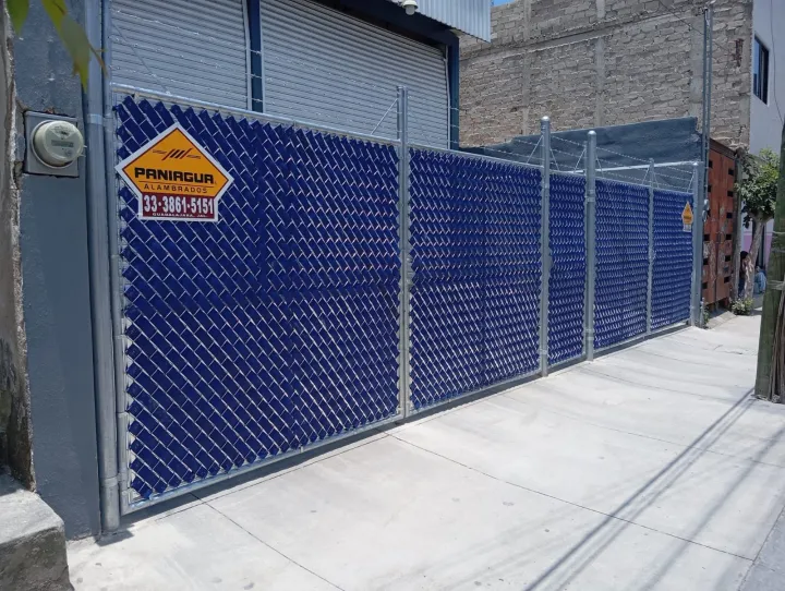 Portón de malla ciclónica con cinta de privacidad azul y placa Paniagua