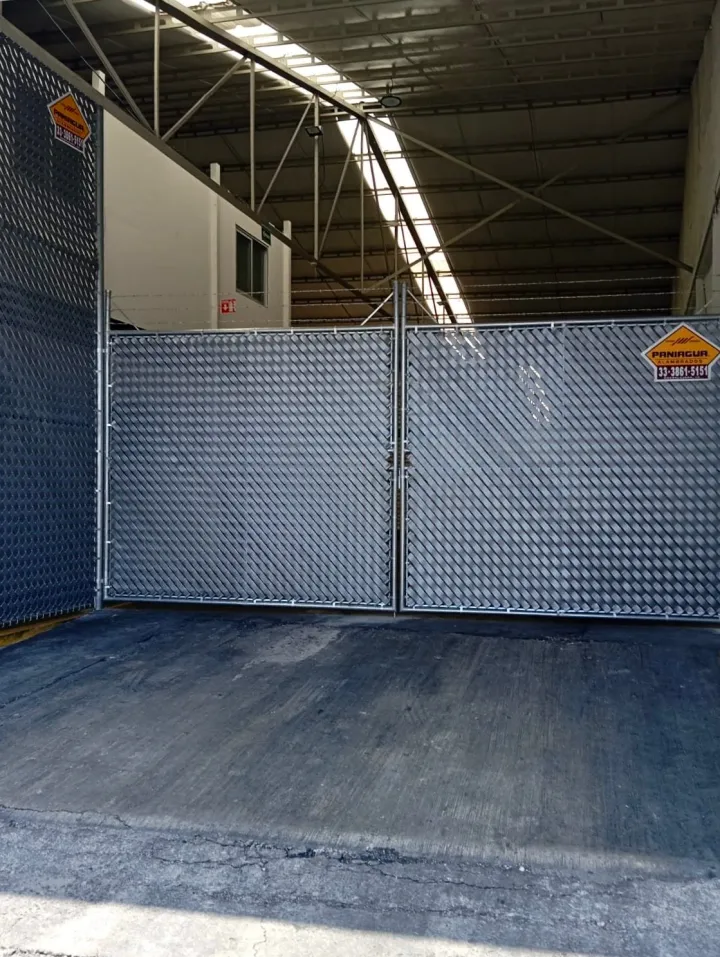 Portón de malla con cinta de privacidad en el acceso de una bodega