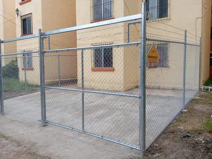 Portón y cerca de malla ciclónica frente a un edificio habitacional